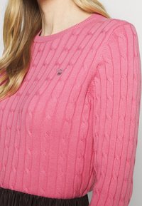 Maglione rosa a maglia con una texture a coste, caratterizzato da un collo rotondo e un piccolo logo sul petto. Progettato per un look aderente.