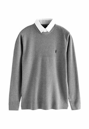 Suéter de punto gris con una camisa blanca de cuello debajo. Presenta puños y dobladillo acanalados, y un pequeño logo negro en el pecho.