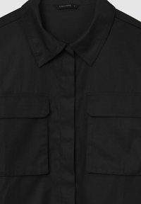 Schwarze Hemdjacke aus glattem Stoff, mit Kragen, zwei Brusttaschen und Schulterakzenten. Einfaches und strukturiertes Design.