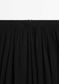 Section de jupe en tissu noir plissé avec une ceinture étroite et une petite fermeture éclair au centre du dos.