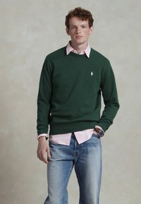 Groene sweatshirt met ronde hals, voorzien van een klein geborduurd logo. Draag het over een lichtroze gestreepte overhemd met knopen en in combinatie met blauwe jeans.
