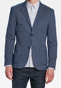 Blå strukturerad kavaj med två framfickor och en knappstängning. Bärs över en ljusgrå skjorta med skräddarsydd passform.