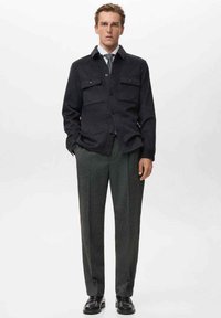 Dunkle Wolljacke mit Knöpfen und zwei Brusttaschen, kombiniert mit strukturierten grauen Hosen und schwarzen Lederschuhen. Einfaches und maßgeschneidertes Design.