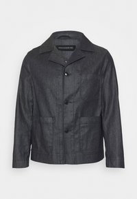 Chaqueta de mezclilla oscura con cuello, botones frontales y dos bolsillos laterales. Presenta un diseño limpio y una tela texturizada. Etiqueta interior visible.