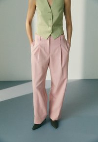 Lys grønn skreddersydd vest med knapper kombinert med høyt liv, plisserte rosa bukser. Modellen har på seg grønne spisse hæler.