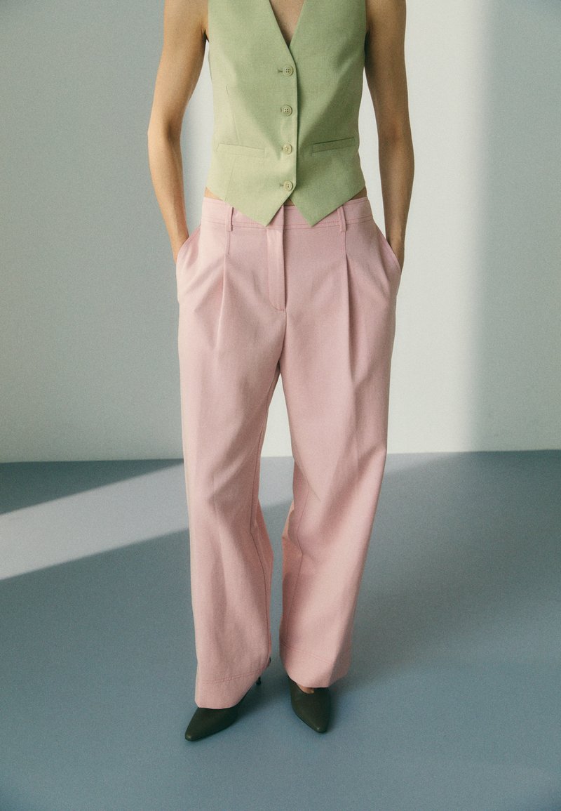 Lys grønn skreddersydd vest med knapper kombinert med høyt liv, plisserte rosa bukser. Modellen har på seg grønne spisse hæler.