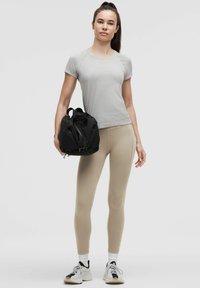 Maglietta grigia chiara a maniche corte, leggings beige e borsa da palestra nera. I leggings sono attillati; la borsa presenta una cerniera e una maniglia.