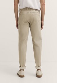 Beige Baumwollhosen mit umgeschlagenen Säumen, Gesäßtaschen und schmalem Schnitt. Getragen mit leichter Fußbekleidung, die einen lässigen Stil zeigt.