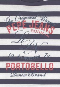 Námořnická a bílá pruhovaná látka s červeným a modrým textem, který zní "Pepe Jeans Portobello London 1973 Denim Brand."