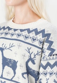 Strickpullover mit Rundhalsausschnitt, in einem Weiß-Blauton gehalten, mit Rentiermustern und geometrischen Akzenten in Blau.