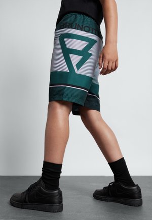 Shorts verts et blancs avec un motif à rayures audacieux, une taille élastique, associés à des baskets et des chaussettes noires.