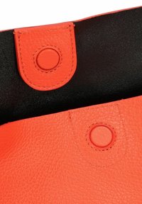 Oranje leder met korrelstructuur en een gladde zwarte binnenkant, voorzien van ronde drukkers en contrasterend stiksel nabij de rand.