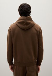 Felpa marrone con cappuccio, con polsini e orlo a coste, dal design semplice e dalla texture morbida, vista dalla parte posteriore su uno sfondo neutro.