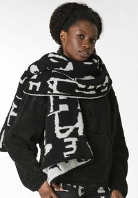 Bufanda con diseño en blanco y negro con patrones abstractos, hecha de material suave, colocada alrededor del cuello, con una textura esponjosa.