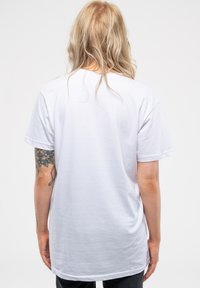 White cotton t-shirt with a relaxed fit and short sleeves, featuring a plain back and visible tattoo on the left arm.