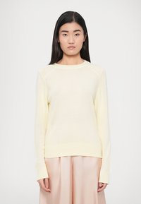 Ανοιχτό κίτρινο πλεκτό πουλόβερ με μακριά μανίκια, ριμπ μανσέτες και τελείωμα. Διαθέτει στρογγυλή λαιμόκοψη και υφασμάτινες λεπτομέρειες στους ώμους.