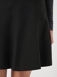 Musta liehuva hame sileällä tekstuurilla, jossa on saumadetaljit ja polven pituinen leikkaus. Kangas vaikuttaa joustavalta ja kestävältä.