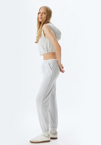 Grijze cropped hoodie met een capuchon, gecombineerd met grijze joggingbroeken met elastische boorden en zakken, aangevuld met witte sneakers.