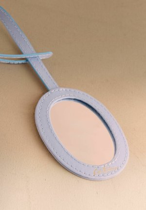 Ovaalne käeshoitav peegel helesinise õmmeldud raamiga ja sangaga, mis peegeldab beežikat pinda, asetatud sobiva beežika tausta peale.