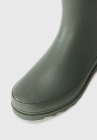 Stivale in gomma verde con una texture liscia, punta arrotondata e suola a profilo basso. Presenta una leggera lucentezza e un design dell'upper continuo.