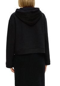 Zwarte cropped hoodie gemaakt van zachte stof, met een grote capuchon en lange mouwen. Gladde textuur met een eenvoudig, strak ontwerp.