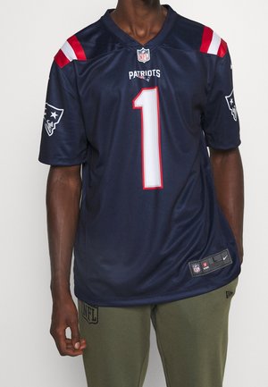 Man wearing navy blue New England Patriots NFL jersey with red and white accents and number 1, paired with olive green pants.