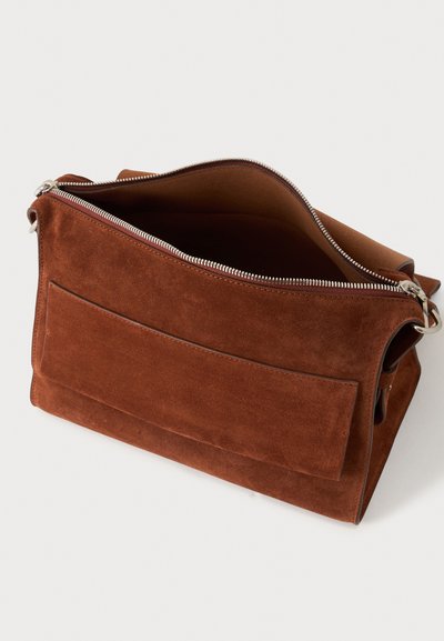 Sac à épaule en daim marron avec fermeture éclair argentée, poche avant plate et compartiment principal ouvert sur fond clair.