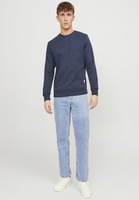 Marine crew neck sweatshirt van zacht materiaal, gecombineerd met lichtblauwe rechte jeans en witte sneakers. Eenvoudig ontwerp met ribgebreide manchetten.