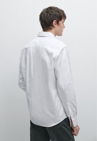 White long-sleeve shirt with a standard collar and button cuffs, made of smooth fabric, featuring a central back seam and classic fit.