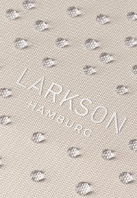 Primer plano de tela beige con puntos blancos en relieve y el texto "LARKSON HAMBURG" impreso en blanco.