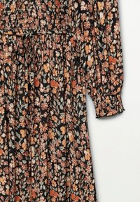 Robe fleurie en tissu noir avec des fleurs orange et blanches. Elle présente un corsage froncé, de longues manches bouffantes et un lien à la taille.
