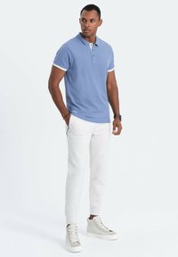 Ljust blå polo skjorta med flat krage, vit kant, tillsammans med vita smala byxor och grå höga sneakers. Slät tygtextur.