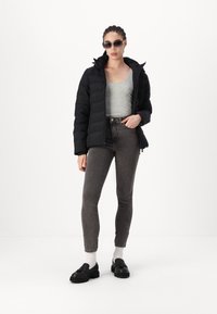 Doudoune noire, débardeur gris, jeans taille haute gris foncé, mocassins noirs, chaussettes blanches, lunettes de soleil ; tissu lisse, coupe décontractée.