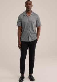 Camisa de manga corta con cuello en una tela gris texturizada, con un frente abotonado; combinada con pantalones negros a medida y mocasines negros.