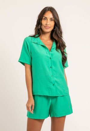 Chemise verte à manches courtes avec boutons à l'avant et col, associée à un short assorti. Le matériau semble léger avec une finition légèrement texturée.