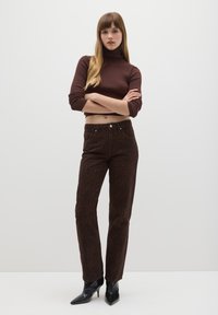 Braunes, geripptes Cropped-Top mit Rollkragen und hochtaillierte braune Hose mit Leopardenmuster, fünf Taschen und Knopfverschluss, kombiniert mit schwarzen Stiefeletten mit Absatz.