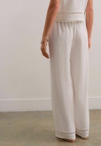 Ensemble en lin blanc constitué d'un haut texturé avec une finition en pompons et d'un pantalon large avec une couture décorative à l'ourlet.