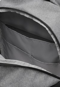 Interno di uno zaino di tessuto grigio con una fodera liscia. Contiene diverse tasche, una delle quali ospita un dispositivo nero. Chiusura a zip nella parte superiore.
