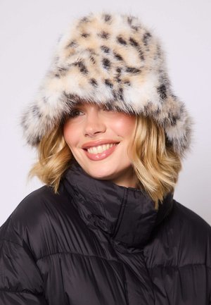 Faux fur bucket hat in beige and black leopard print. Soft texture, wide brim, and rounded top design, worn with a black puffer jacket.
