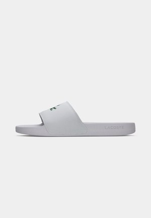 Sandal en slide gris clair avec une large sangle présentant un logo vert. Texture lisse, semelle plate et design minimaliste, convenant pour un usage décontracté.