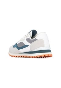 Zapatilla colorida que presenta una combinación de materiales en blanco, gris y teal. Texturas de malla y gamuza con una suela de goma y un patrón de un grosor notable.