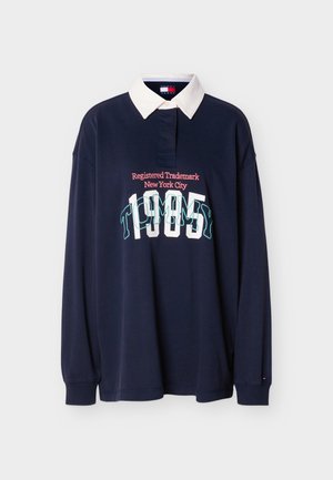 Tmavě modré polo tričko s dlouhým rukávem a bílým límcem. Na tričku je grafický potisk s nápisem „TOMMY“ a „Registered Trademark New York City“ v kontrastních barvách.