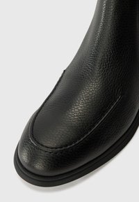Botte en cuir noir avec une finition texturée, un bout arrondi lisse, des coutures détaillées et une semelle en caoutchouc noir slim.