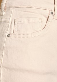 Tecido de denim rosa claro com um bolso frontal, costuras finas e um detalhe de botão metálico. Acabamento suave e texturizado com ligeira elasticidade.
