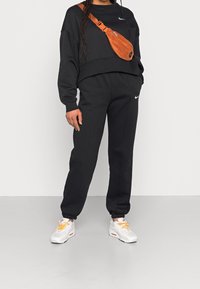 Black cropped sweatshirt and matching joggers, paired with white sneakers featuring orange laces. A brown crossbody bag is worn across the shoulder.