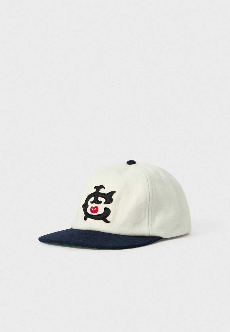 Hvid baseballkasket med mørkeblå skygge og broderet sort og rød stiliseret dyrelogo på frontpanelet, vist på hvid baggrund.