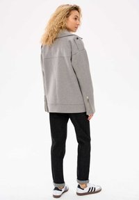 Szary, oversize'owy żakiet z zaokrąglonym dołem, zamkami po bokach oraz guzikami na ramionach, połączony z ciemnymi, slim-fit spodniami i białymi sneakersami.