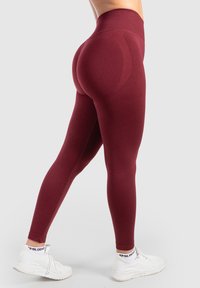 Bordeaux hoge taille leggings met een gladde textuur en een aansluitend ontwerp, voorzien van naaddetails en een taps toelopende enkel, gecombineerd met witte sneakers.