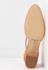 Chaussure en cuir orange à bout pointu, à dos ouvert et à petit talon. La semelle est lisse, avec le nom de la marque et la taille imprimés à l'intérieur.