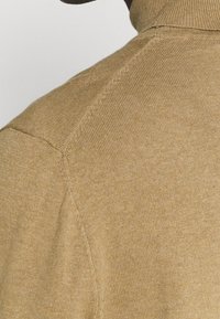 Strick-Turtleneck-Pullover in hellbeige, mit gerippter Textur, nahtlosem Schulterdesign und figurbetontem Schnitt.